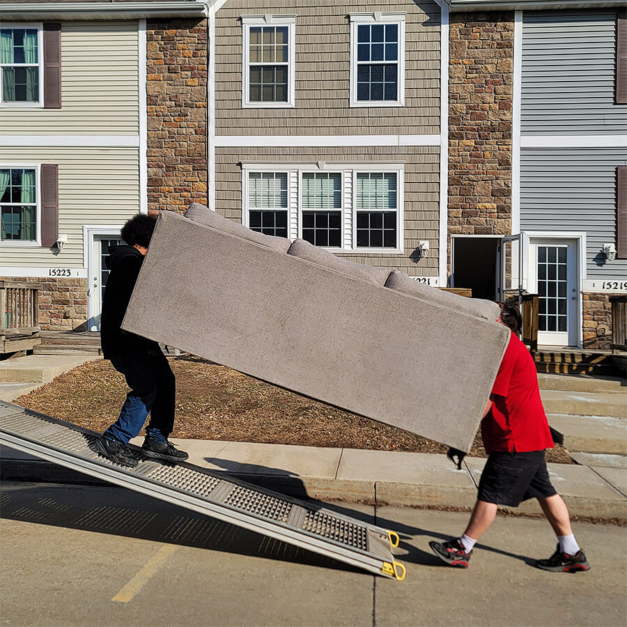 movers are moving a sofa from the residential property in the moving truck in front of a house